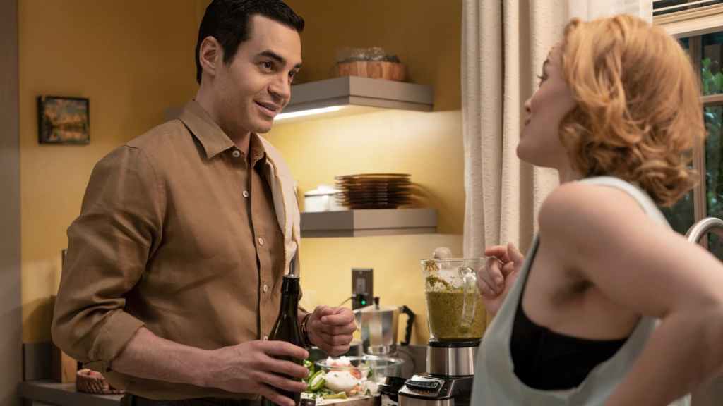 Ramon Rodriguez as Will Trent holding a bottle in a kitchen. He is smiling and looking at Erika Christensen as Angie Polaski who is looking at him.
