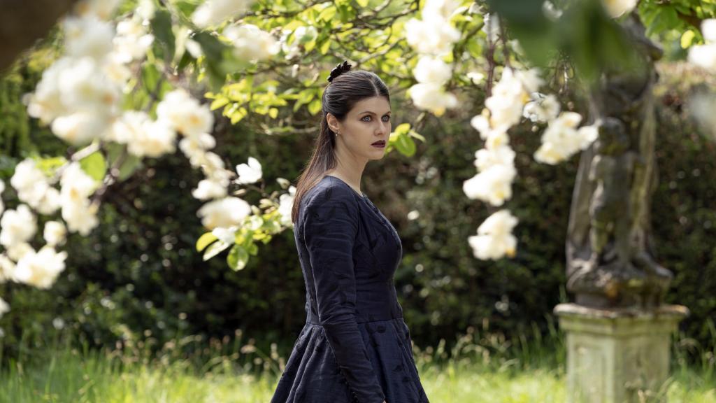 Alexandra Daddario as Dr. Rowan Fielding in Mayfair Witches Season 2. She's in a garden in a dark blue long-sleeve dress looking off in the distance.