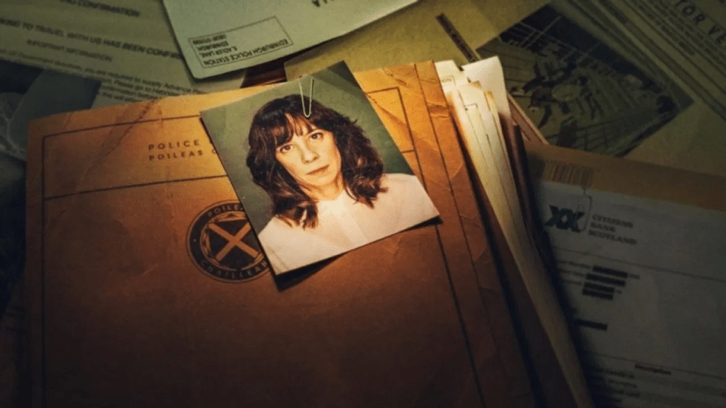 A still image from Dept. Q season one featuring police case files with the picture of a dark-haired woman on top of one of the files