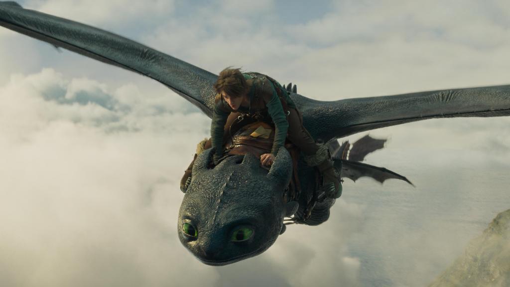 A promotional still from How to Train Your Dragon live-action movie featuring a dragon (Toothless) in flight with his ridder (Mason Thames as Hiccup).