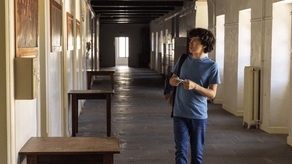 Still image from the movie Le Panache (2024) featuring Joachim Arseguel as Colin in a hallway, holding a piece of paper in his hand while looking at a door.