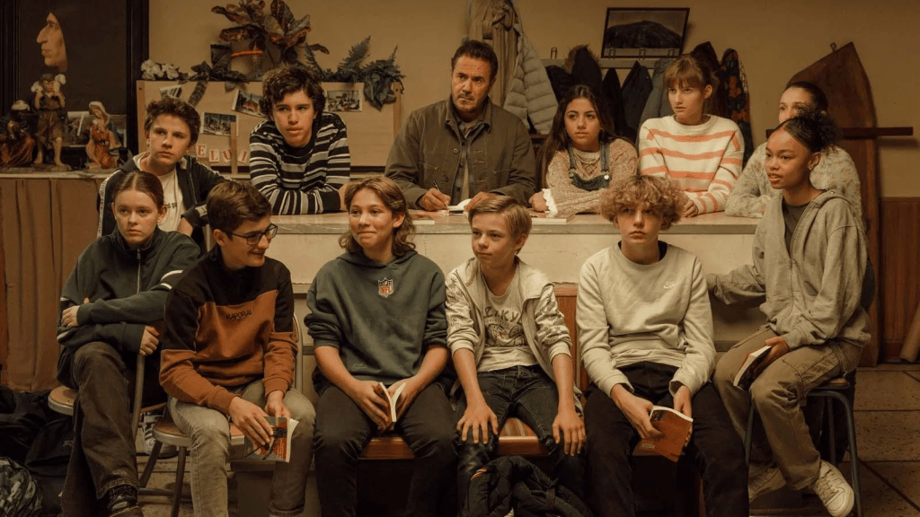 Still image from the movie Le Panache (2024) featuring José Garcia as M. Devarseau surrounded by middle school age kids.
