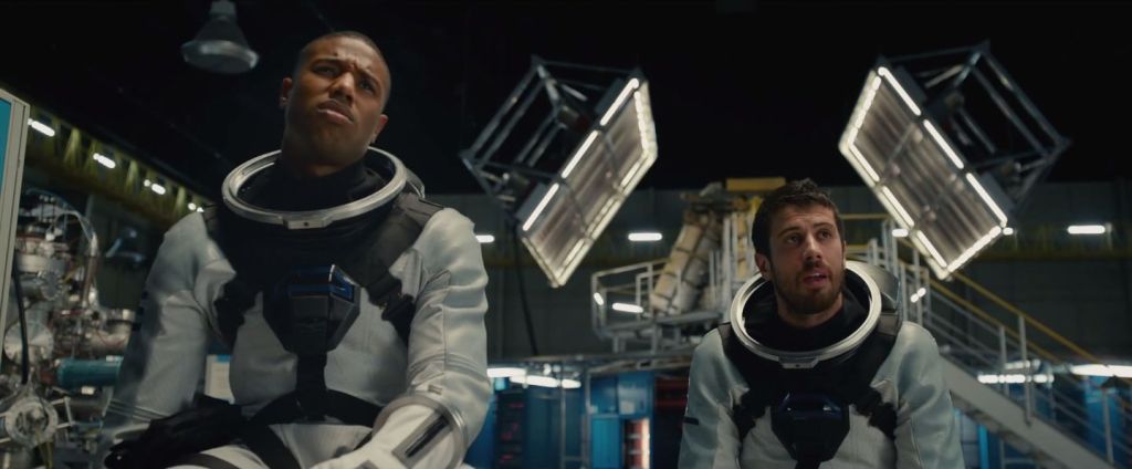 A still from 2015's Fantastic Four movie featuring Michael B. Jordan as Johnny Storm, and Toby Kebbell as Victor Von Doom both wearing a space suit without the helmet. Behind them some kind of lab.