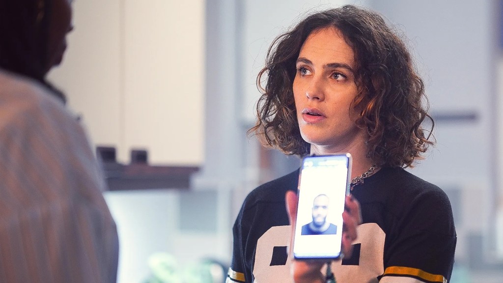 Still of Jessica Brown Findlay in 'The Flatshare (2022)', she's holding a phone showing the picture of a black man to a woman.