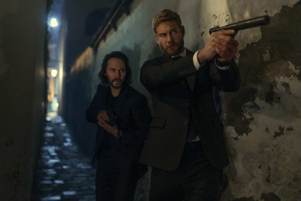 Taylor Kitsch and Tom Hopper in The Terminal List: Dark Wolf (2025). They are dressed in dark suits, both holding guns with silencers advancing in an alley at night.