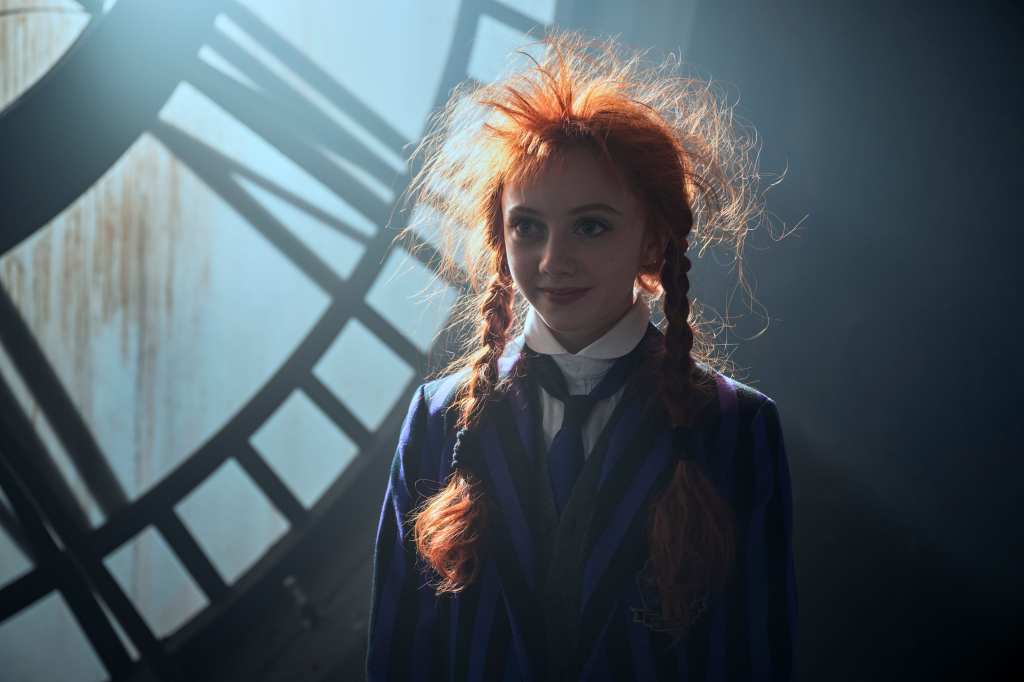 Evie Templeton dressed in Nevermore purple and black stripped uniform, with her red frazzled hair in Wednesday season 2.