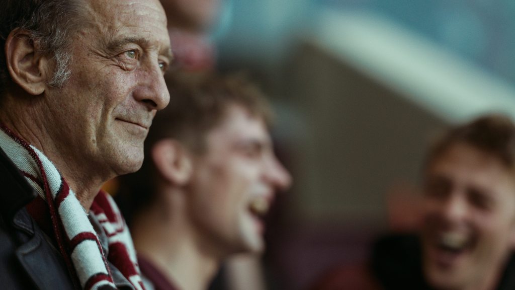 A smiling older man looking in the distance, he's wearing