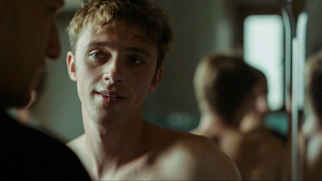 A shirtless young man in what looks to be a bathroom, talking to another man, a scene from The Quiet SOn.