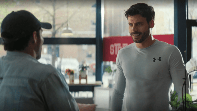 Scott Hunter (François Arnaud) wearing a gray skintight Under Armour shirt, smiles at Kip wearing a baseball cap at his barista job.