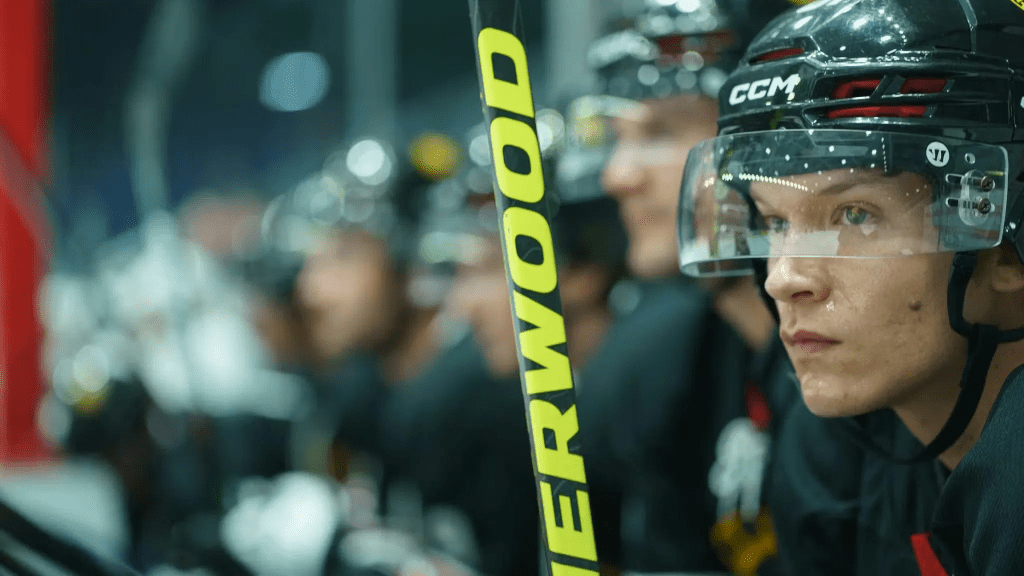 Ilya Rozanov (Connor Storrie) in his hockey uniform looking focused, seated on a bench during a game.