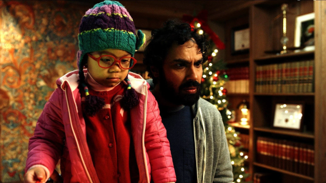 Jordyn McIntosh as Maya stand in front of Kunal Nayyar as A.J. Fikry, with a decorated Christmas tree and bookshelves in the background.